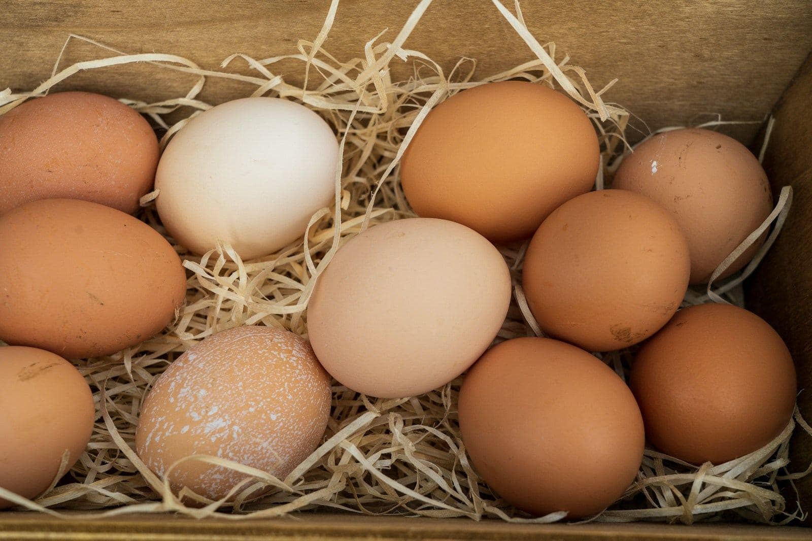 Brown and white eggs nested in straw in a wooden box
